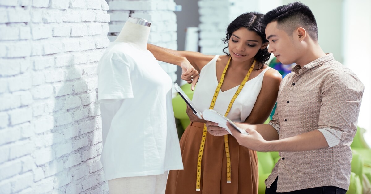  A young woman and a young man are discussing fabric swatches while standing next to a mannequin.